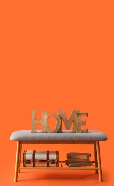 Soft bench with decor, books and suitcase on orange background