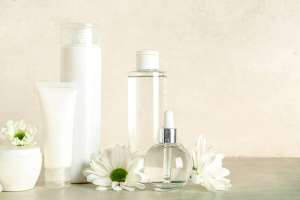 Различные косметические средства и ромашковые цветы на столе на светлом фоне