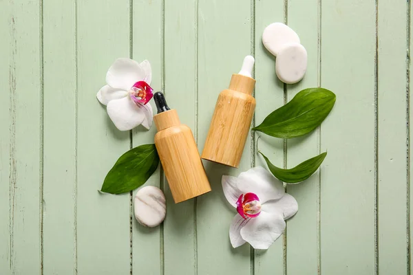 Composition with bottles of cosmetic products, spa stones and orchid flowers on color wooden background