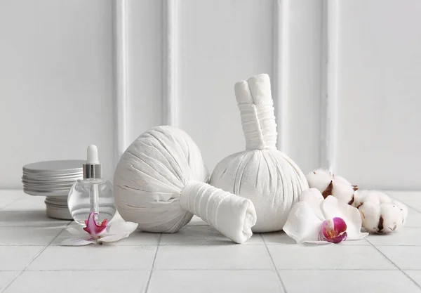 Herbal massage bags, cosmetic products and flowers on light tile table