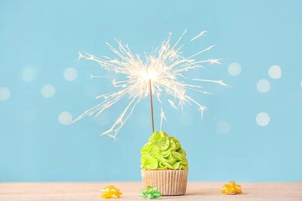 Tasty birthday cupcake with sparkler and decor on color background