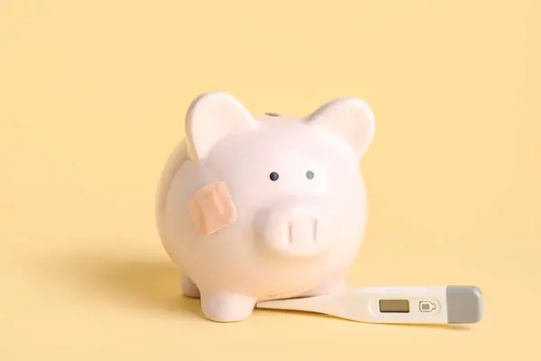 Piggy bank with digital thermometer on beige background