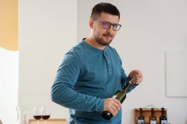 Genç şarap garsonu mutfakta şarap şişesi açıyor.