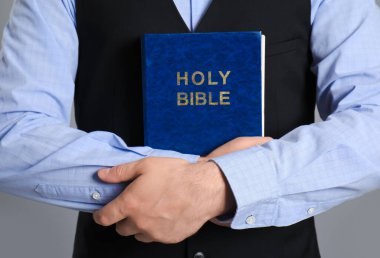 Gri arka planda İncil 'i olan genç adam, yakın plan.