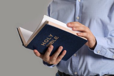 Gri arka planda İncil okuyan genç adam, yakın plan.