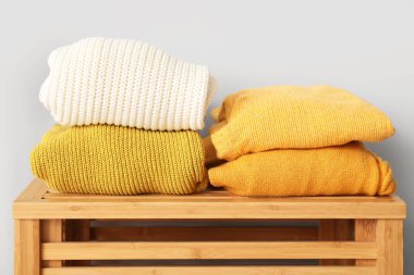 Kalın giysi yığını ahşap masada, ışık duvarının yanında, yakın plan.