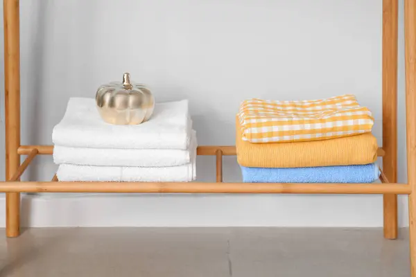 Rack with clean towels and decor near light wall
