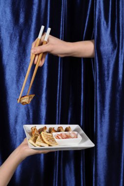 Lezzetli Çin yemekleri ve yemek çubuklarıyla renkli kumaş arka planda kadın elleri.