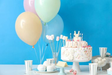 Mavi duvarın yanındaki masada farklı tatlılar olan doğum günü pastası.