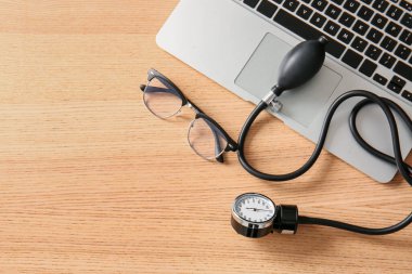 Diz üstü bilgisayarı ve gözlüklü Sphygmomanometre ahşap sağlık masasında, yakın plan.