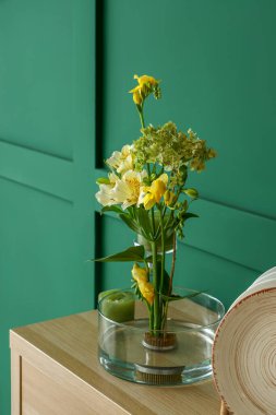 Yeşil duvarın yanındaki rafta mumları olan güzel bir ikebana.