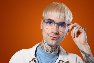 Renkli arka planda gözlüklü genç dövmeli adam, yakın plan.