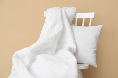 Beyaz battaniyeli sandalye ve bej duvarın yanında yastık.