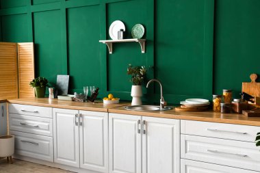 Modern mutfakta okaliptüs dalları, şarap şişesi ve mutfak aletleri olan beyaz tezgah.