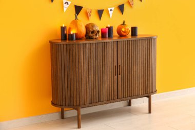 İçi yanan mumlarla dolu çekmeceler Cadılar Bayramı kutlaması için balkabakları, turuncu duvarda kafatası ve bayraklar asılı.