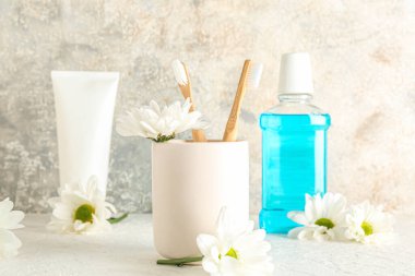 Diş fırçaları, kozmetik ürünleri ve masada papatya çiçekleri olan tutucu.