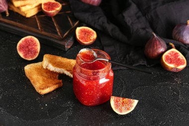 Kavanoz dolusu tatlı incir reçeli ve siyah arkaplanda lezzetli tostlar.