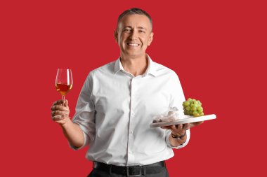 Kırmızı arka planda şarap ve atıştırmalıklarla dolu olgun bir adam.