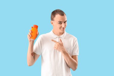 Genç adam mavi arka planda güneş kremini işaret ediyor.