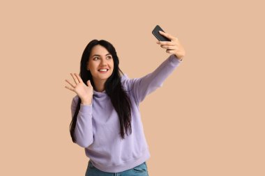 Bej arka planda selfie çeken mutlu genç esmer portresi.
