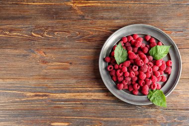 Taze ahududu ve ahşap arka planda yapraklarla dolu bir tabak.