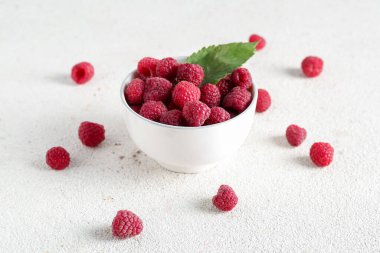 Taze olgun ahududu ve beyaz arka planda yaprak dolu bir kase.