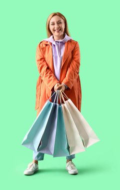 Yeşil arka planda alışveriş torbaları olan ceketli olgun bir kadın.