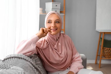Olgun Müslüman kadın evdeki kanepede oturuyor.