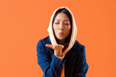 Kapüşonlu genç Asyalı kadın turuncu arka planda öpüşüyor.