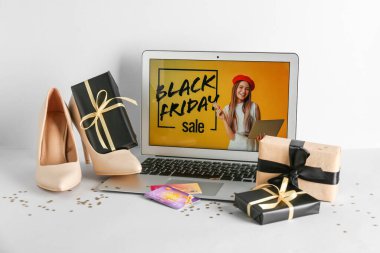 Kara Cuma moda reklamı olan dizüstü bilgisayar, kredi kartları, ayakkabılar ve beyaz arka planda hediye kutuları.