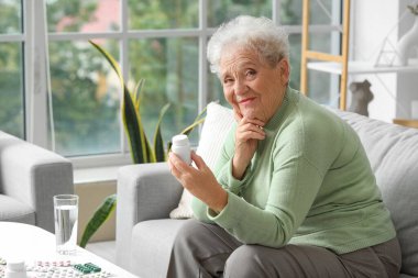 Evde ilaç şişesi olan düşünceli bir yaşlı kadın.