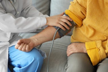 Doktor evde yaşlı bir kadının kan basıncını ölçüyor.