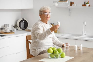 Mutfakta ilaç şişesi olan yaşlı bir kadın.