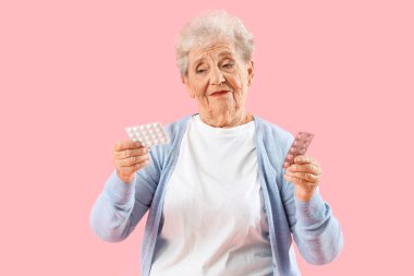 Pembe arka planda hapları olan yaşlı bir kadın.