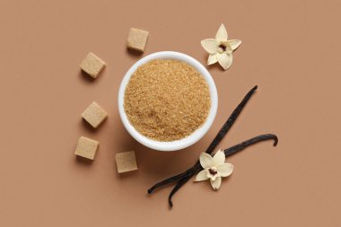 Kahverengi arka planda aromatik vanilya şekeri, çiçekler ve çubuklarla dolu bir kase.