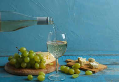Beyaz şarap, cam ve tahtalara dökülüyor mavi ahşap masada üzümlü.