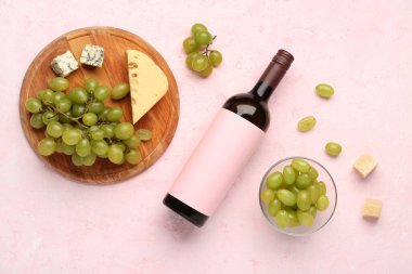Boş etiketli bir şişe lezzetli şarap ve pembe arka planda üzüm.