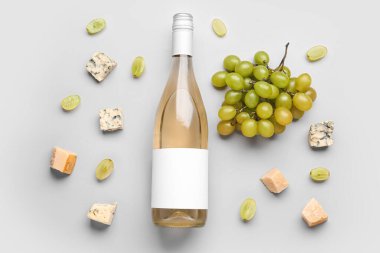 Boş etiketli bir şişe lezzetli şarap ve gri arka planda üzüm.