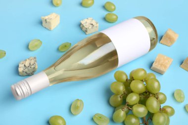 Boş etiketli bir şişe lezzetli şarap ve mavi arka planda üzüm.