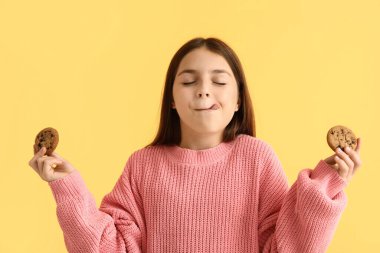 Sarı arka planda tatlı çikolatalı kurabiyeler tutan küçük kız