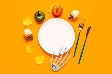 Kafatasları ve turuncu arka planda sonbahar dekoru olan Cadılar Bayramı masası.