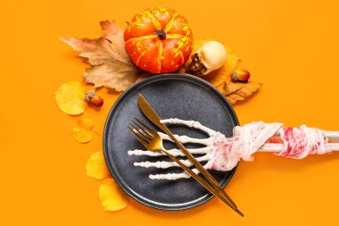 İskelet elli Cadılar Bayramı sofrası ve turuncu arka planda sonbahar dekoru.