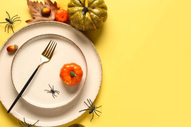 Sarı arka planda balkabakları, örümcekler ve sonbahar yapraklarıyla Cadılar Bayramı sofrası