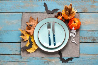 Mavi ahşap arka planda balkabakları, sonbahar yaprakları ve Cadılar Bayramı süslemeleri olan masa ayarı