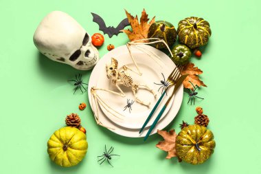 Yeşil arka planda iskelet, kafatası ve sonbahar dekoru olan Cadılar Bayramı sofrası