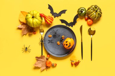 Sarı arkaplanda balkabağı ve Cadılar Bayramı dekoru olan masa ayarları