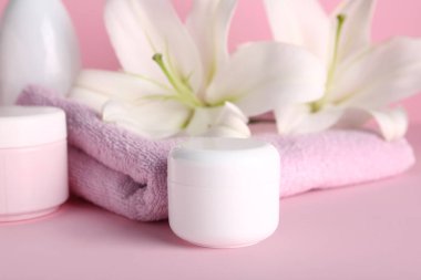 Kozmetik ürünler seti, temiz havlu ve pembe arka planda güzel zambak çiçekleri, yakın plan