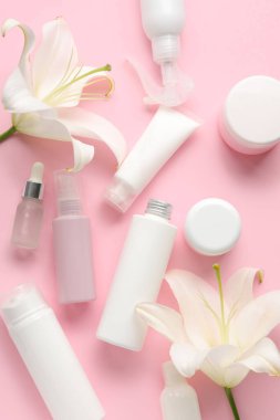 Farklı kozmetik ürünleri ve pembe arka planda zambak çiçekleri olan kompozisyon