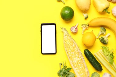 Sarı arka planda sebzeli ve meyveli cep telefonu. Dünya Vegan Günü kavramı