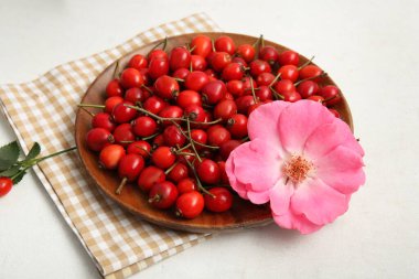 Taze gül kalçası böğürtlenli ahşap tabak ve beyaz arka planda çiçek